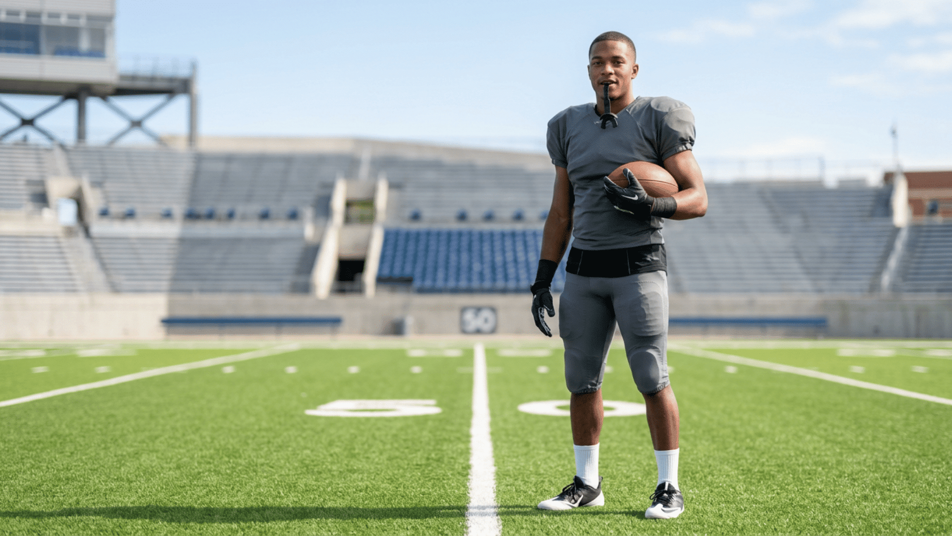 American football player holding a football on a stadium field, representing the ATH football position.