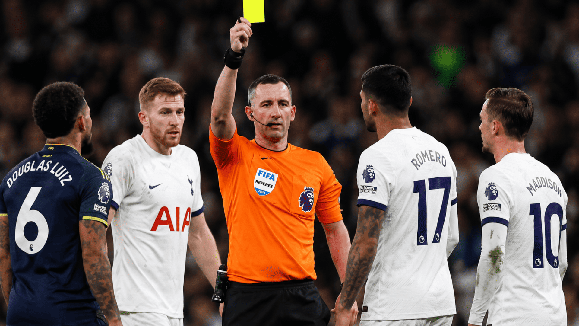 Soccer referee displaying a yellow card while players from opposing teams gather around during a match