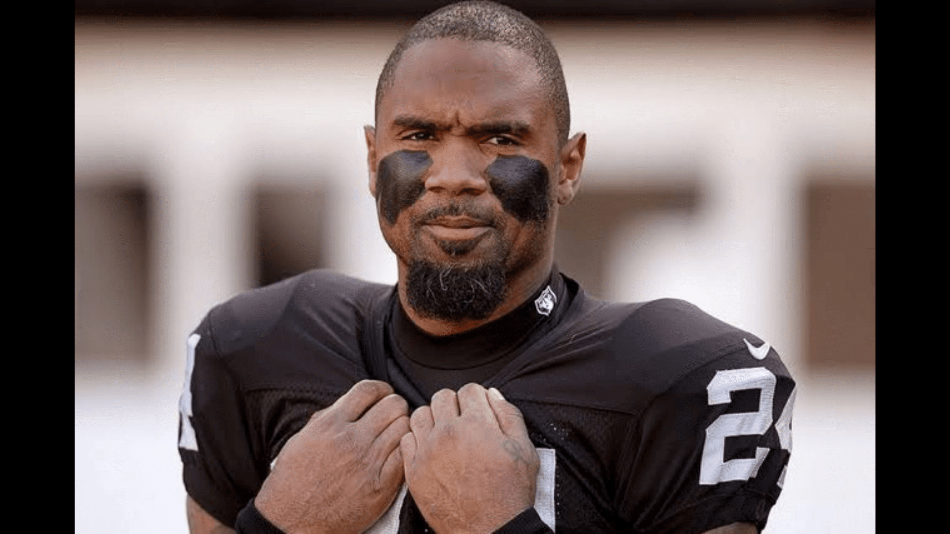 a football player in a black number 24 jersey with eye black holds his collar while looking at the camera