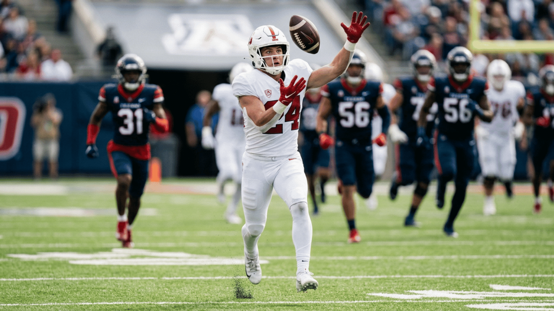 a football player in a white uniform reaches to catch a pass while defenders chase behind on the field