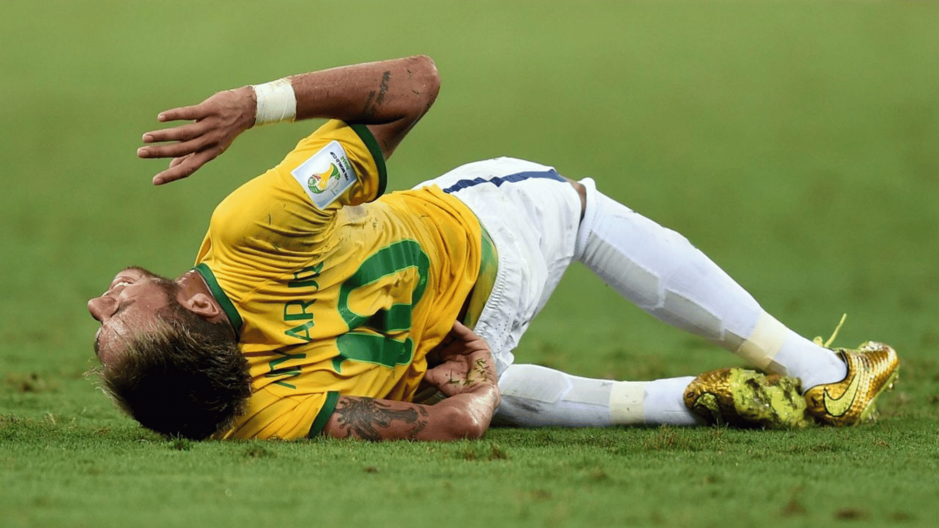 a football player in a yellow kit lies on the grass holding his side after falling during a match on the pitch