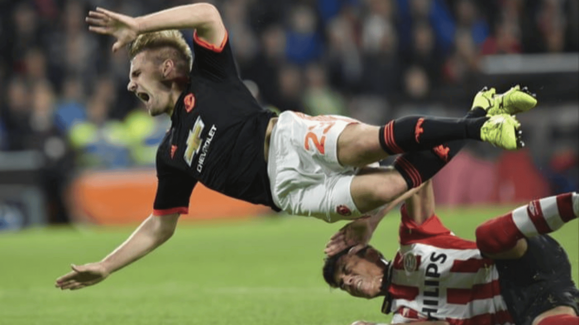a football player in black is sent flying over an opponent in red and white stripes during a dramatic tackle