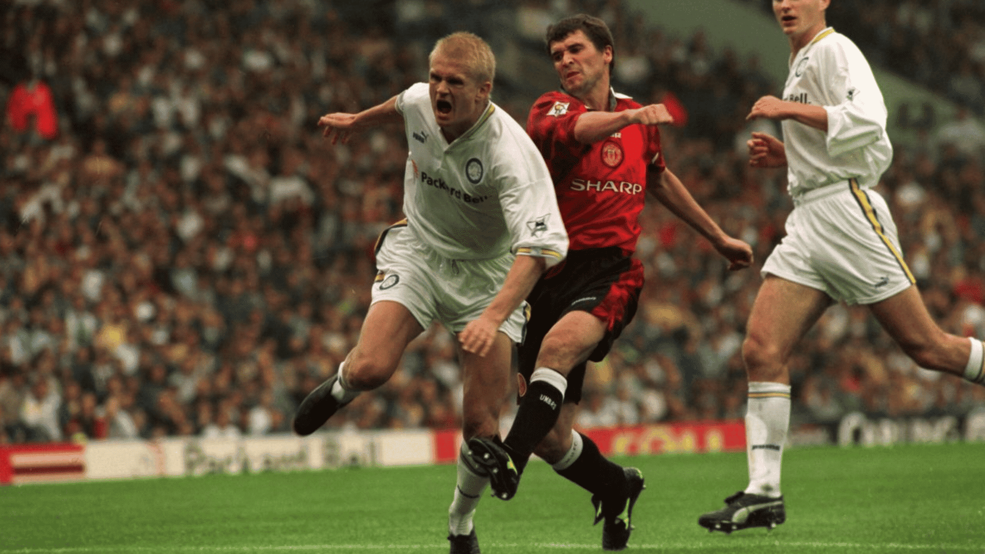 a football player in white is knocked off balance by a red shirted opponent during a match in a crowded stadium