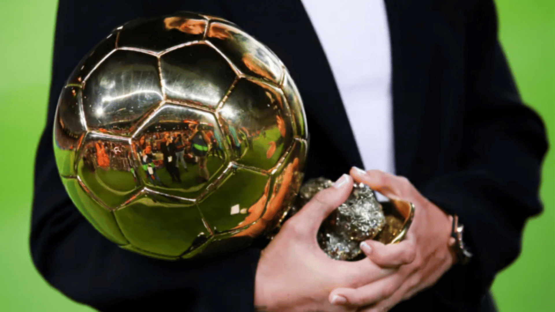 a person in a black jacket holds a golden soccer ball and a piece of pyrite
