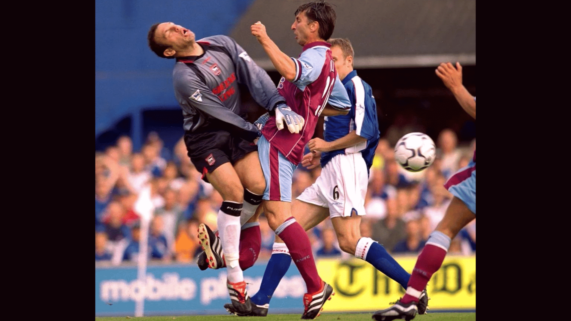 a soccer goalkeeper collides with an outfield player in claret and blue kit during a match with ball nearby