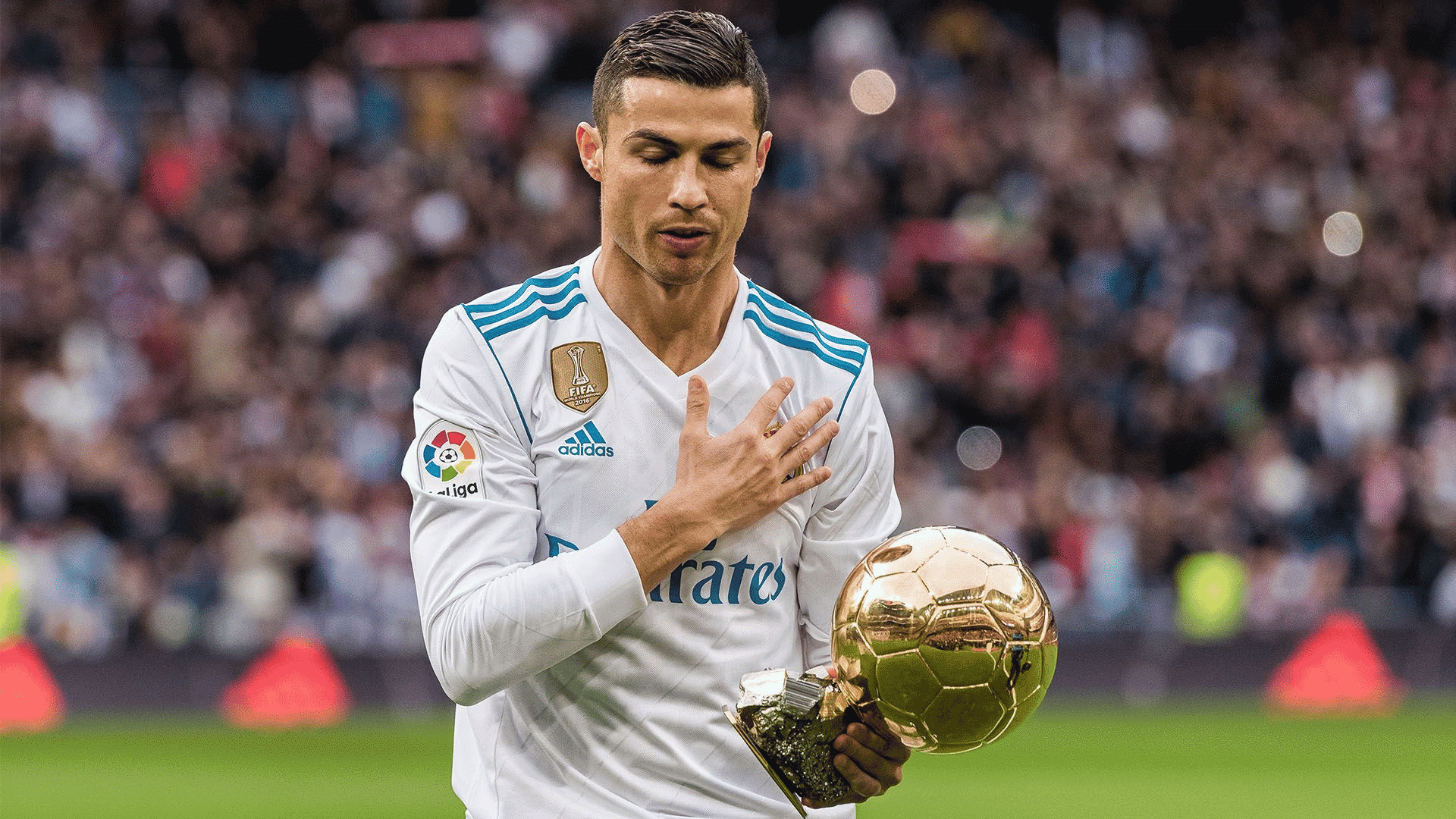 a soccer player in a white jersey holds a golden trophy while placing one hand on his chest before a crowd