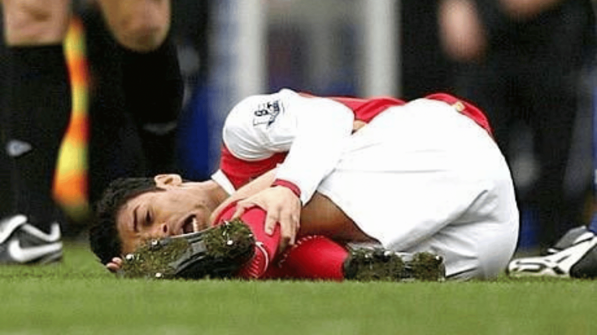 a soccer player in red and white kit lies on grass clutching his leg in pain during a match