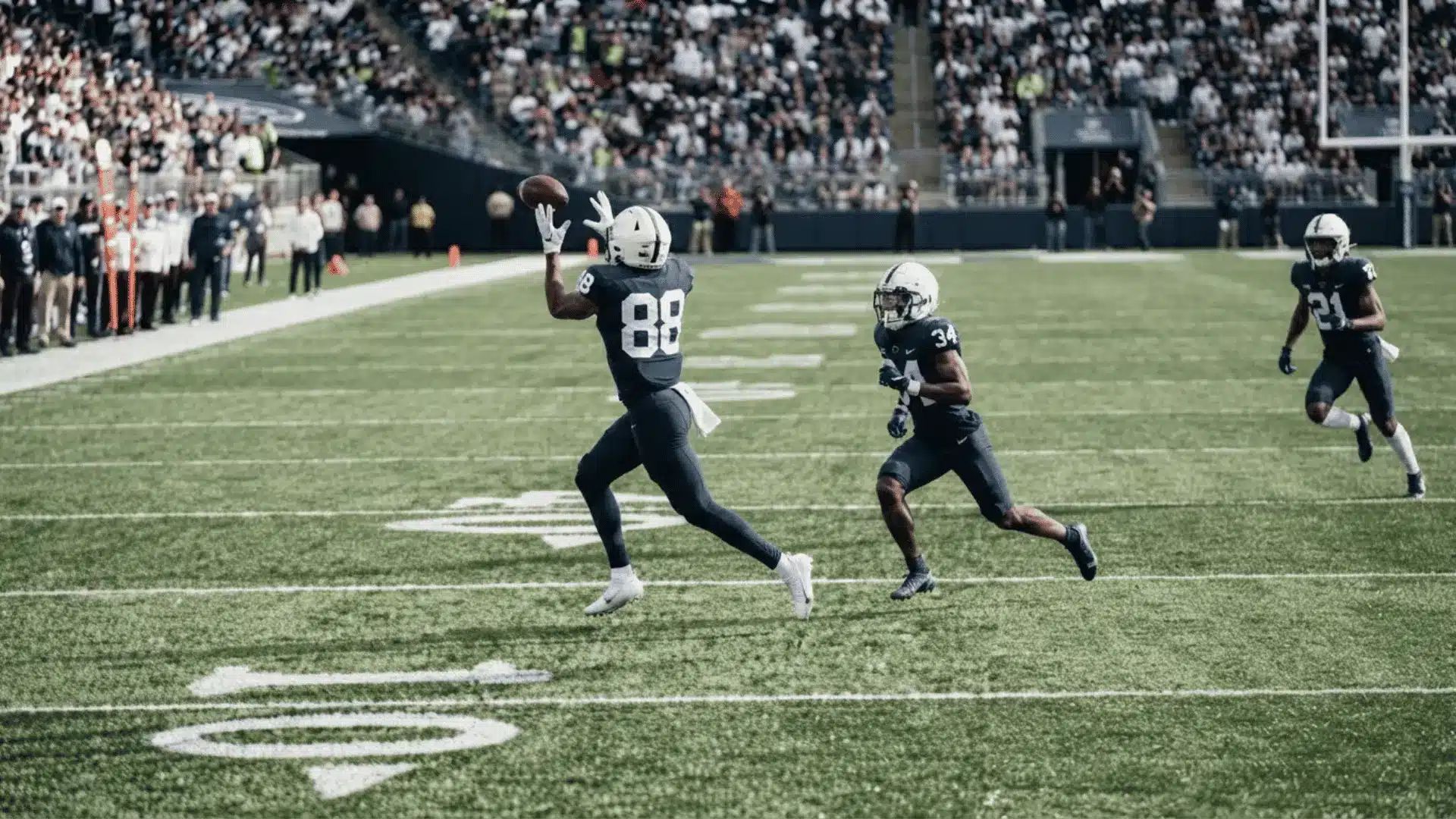 a football receiver in a dark uniform reaches for a pass while two defenders trail across a crowded stadium field