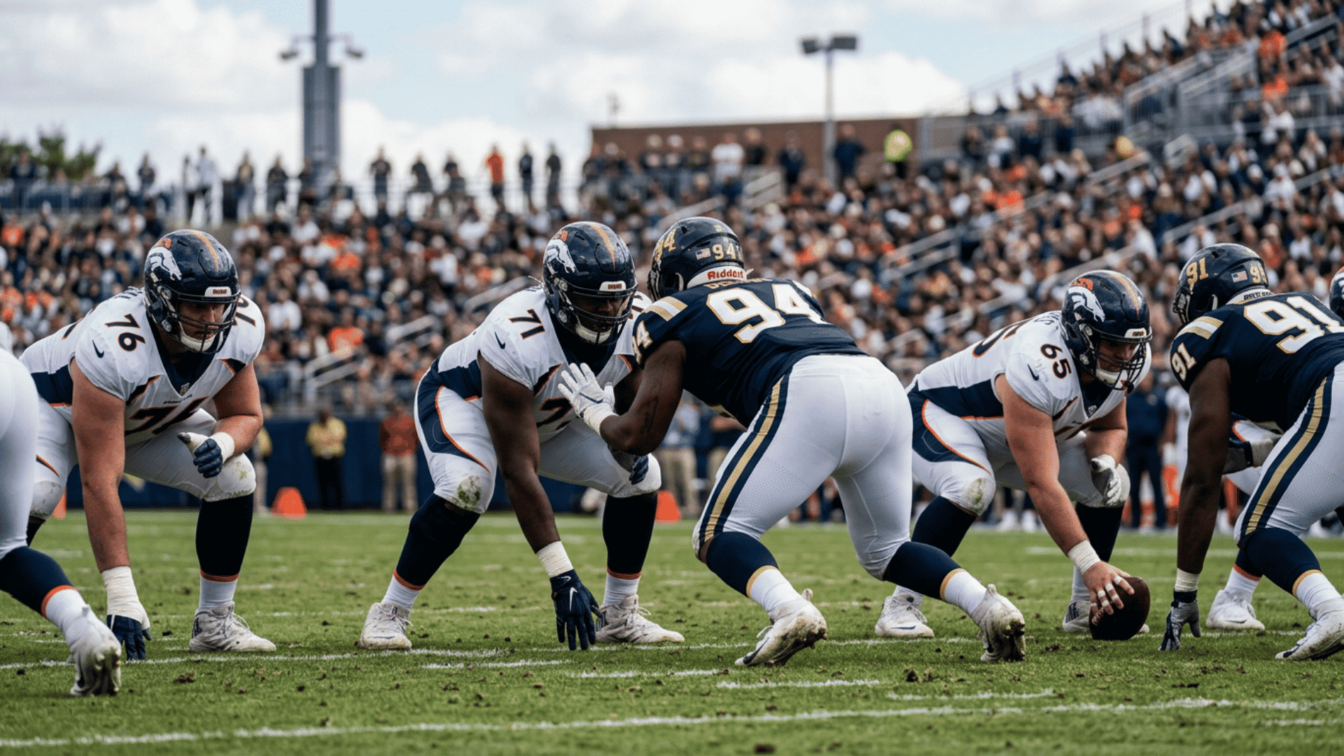 american football offensive and defensive linemen crouched at line of scrimmage in stadium with crowd in background