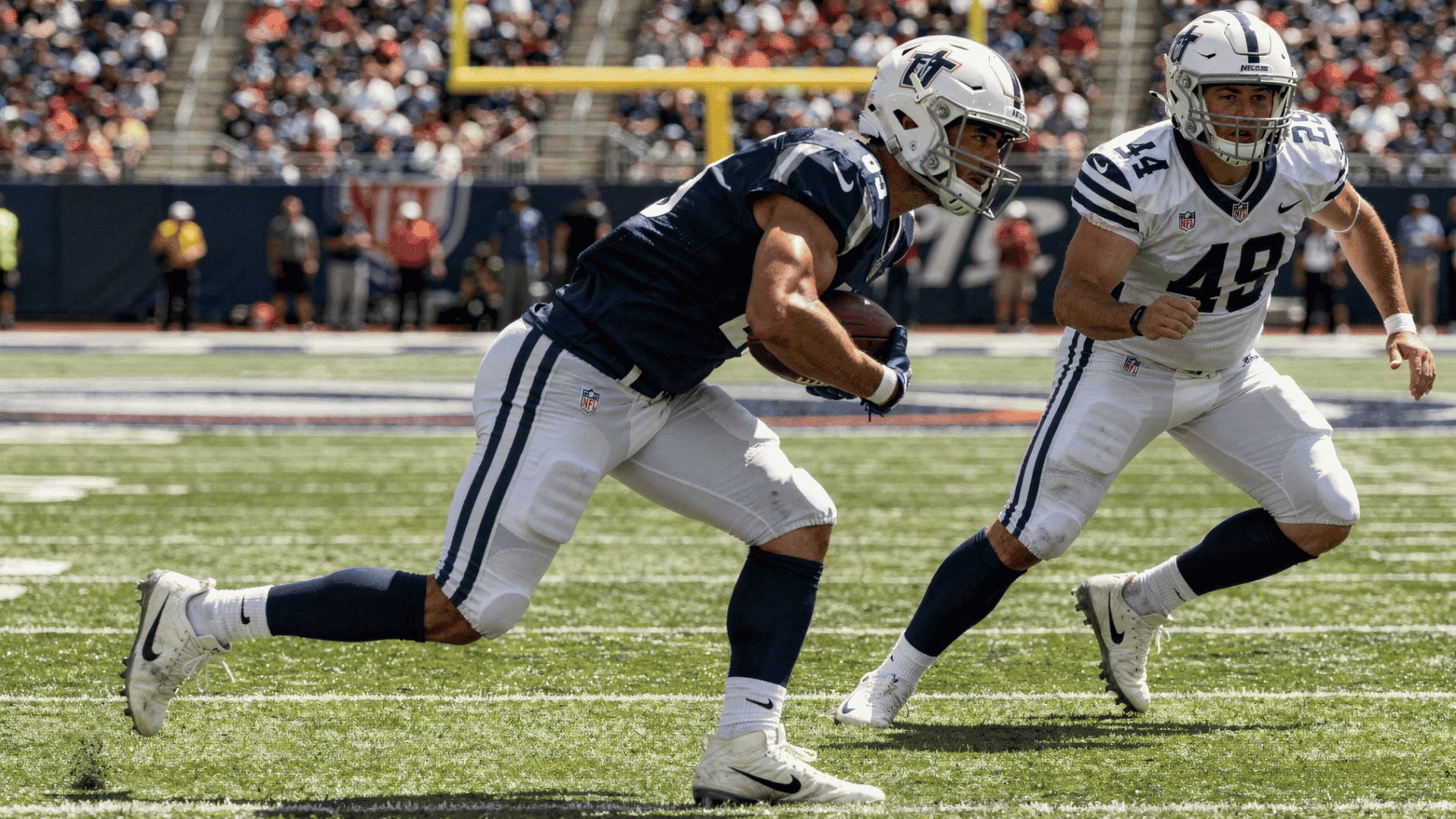 american football player in a blue and white uniform runs with the ball with another player in a white uniform numbered