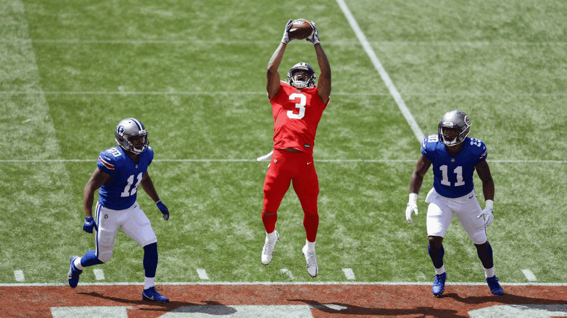 american football player in a red jersey jumps to catch a ball with two players in blue jerseys on either side of him