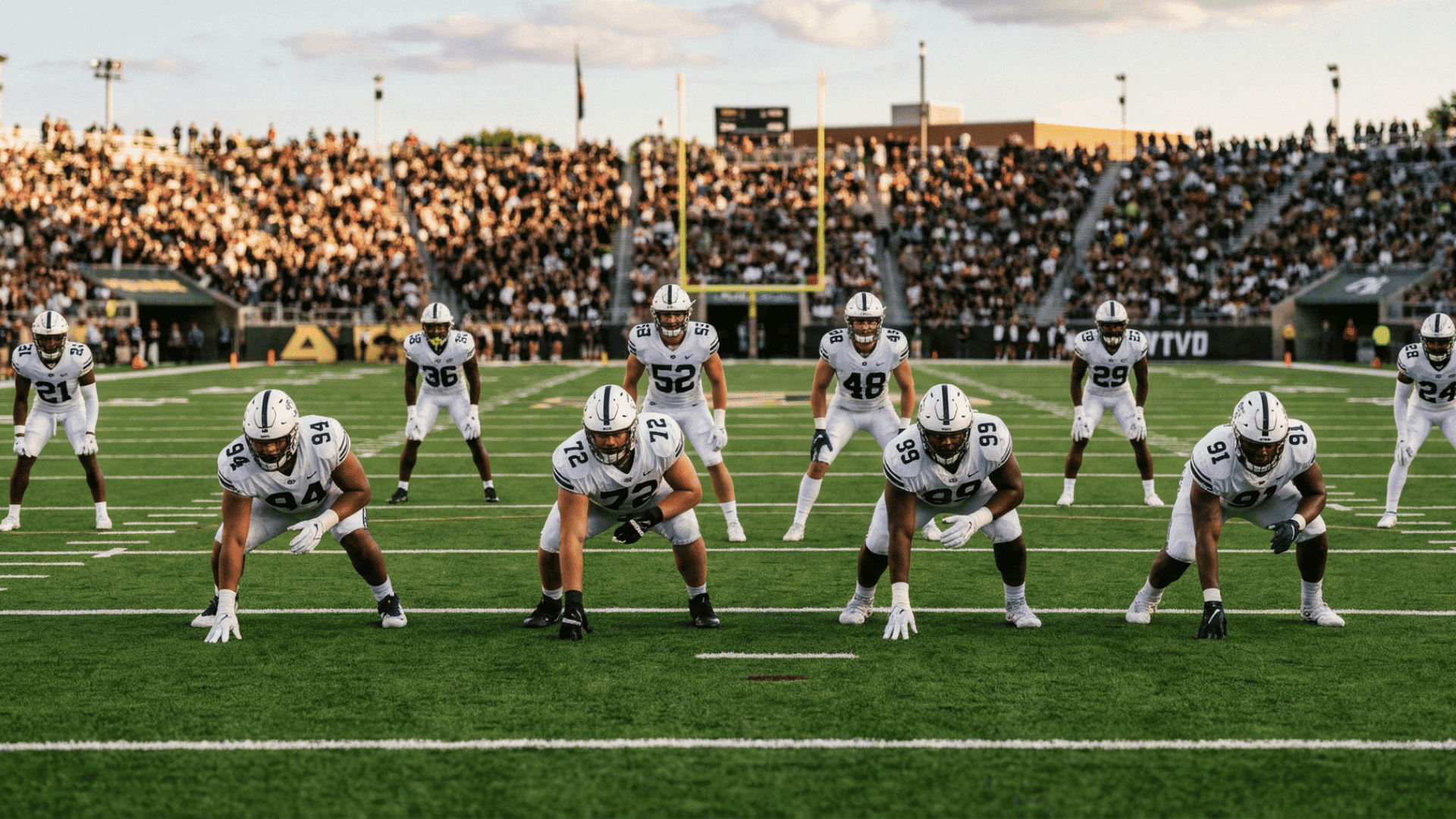 american football players lined up at line of scrimmage during a game in a stadium with large crowd in background