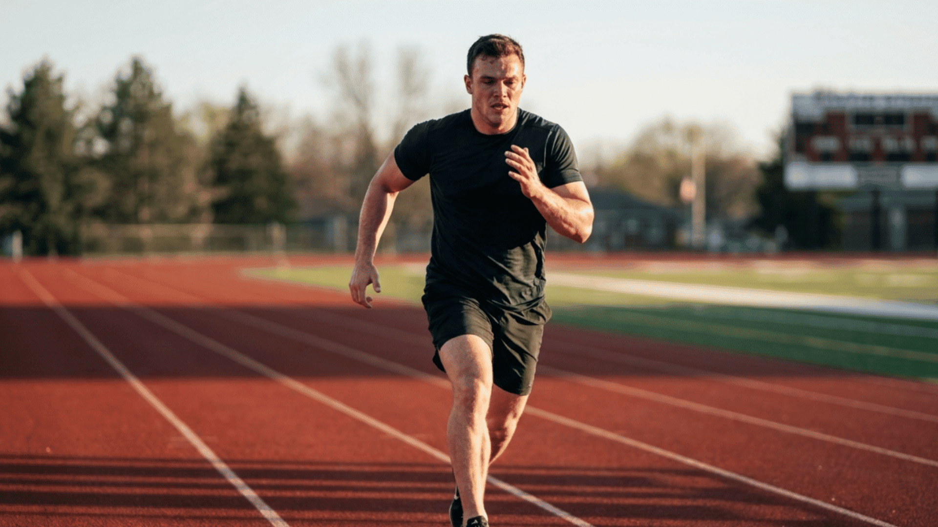 athlete running interval sprints on an outdoor red running track in late afternoon light