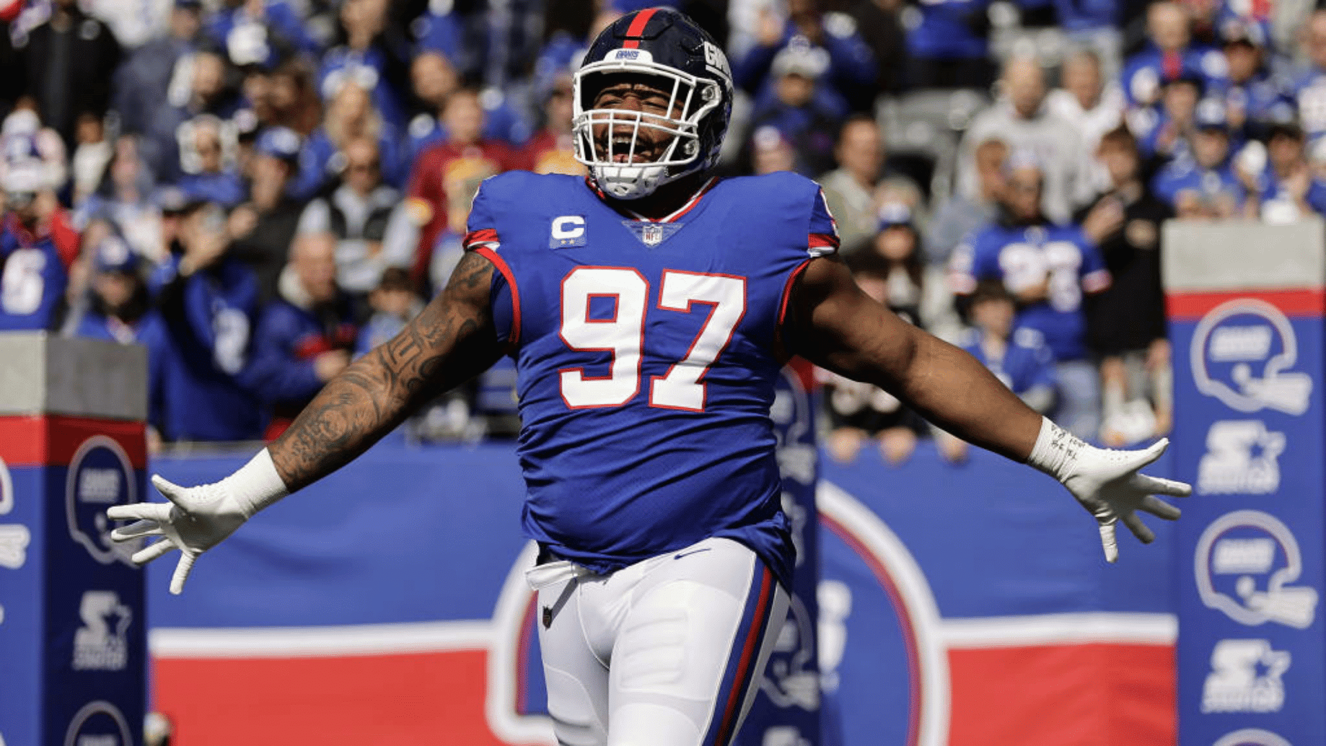 blue jersey number ninety seven celebrating a touchdown with his arms to the side and up in the air wearing required football equipment
