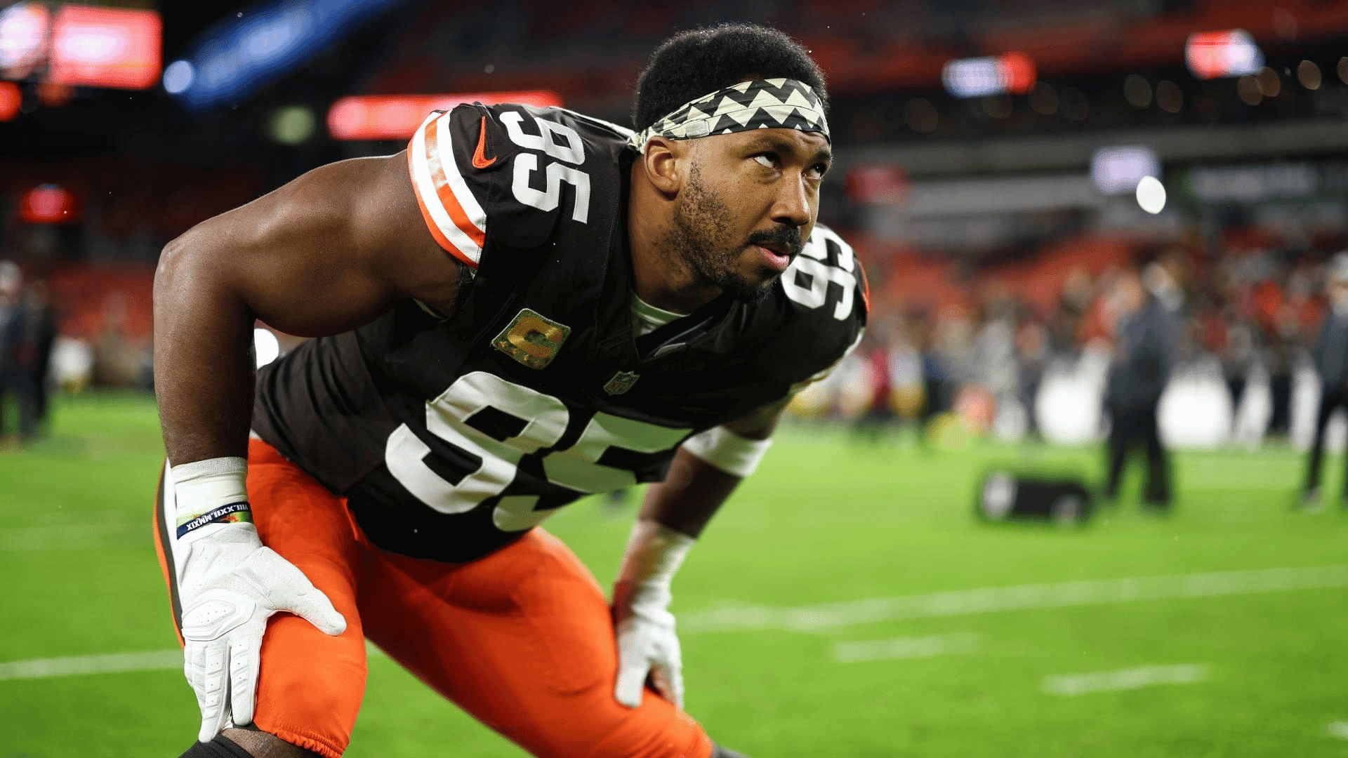 brown jersey number ninety five and oragne shorts preparing for huddle against the opponent and making eyes with the opponents while people are working in the background