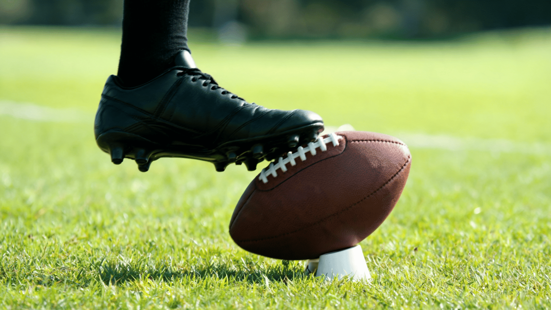 close side view of the firm top of a kicking shoe contacting the lower middle of an american football