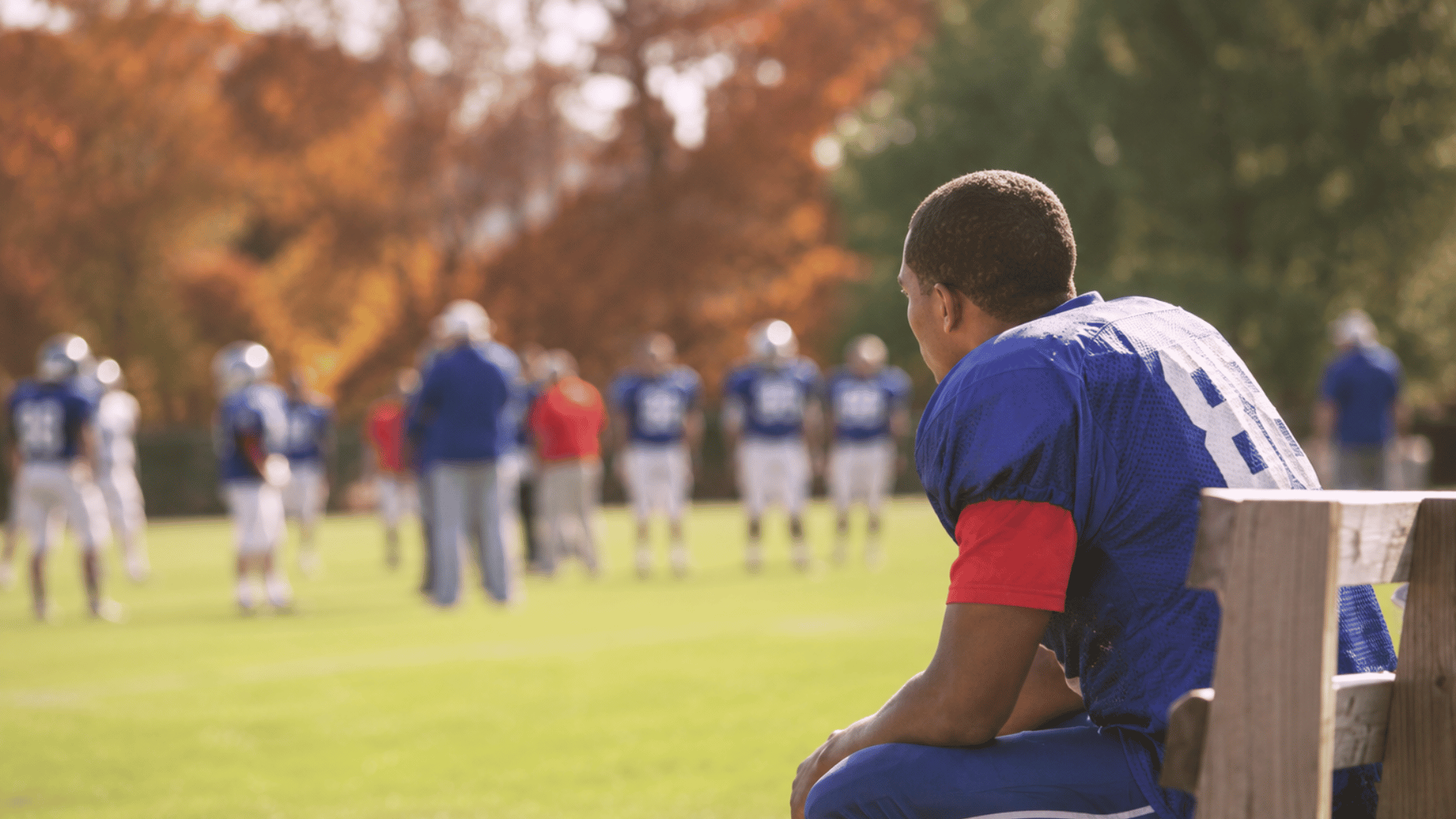 college football athlete observing practice drills from the sidelines while teammates train on the field