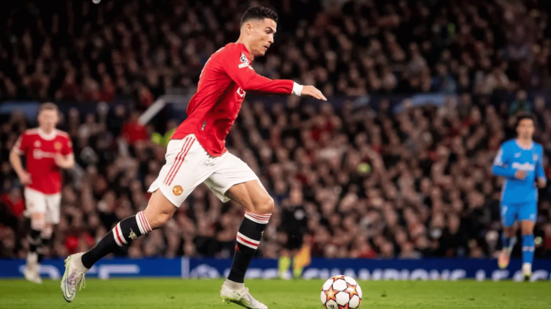 cristiano ronaldo taking a shot on the pitch wearing a red manchester united jersey in front of a blurred stadium crowd