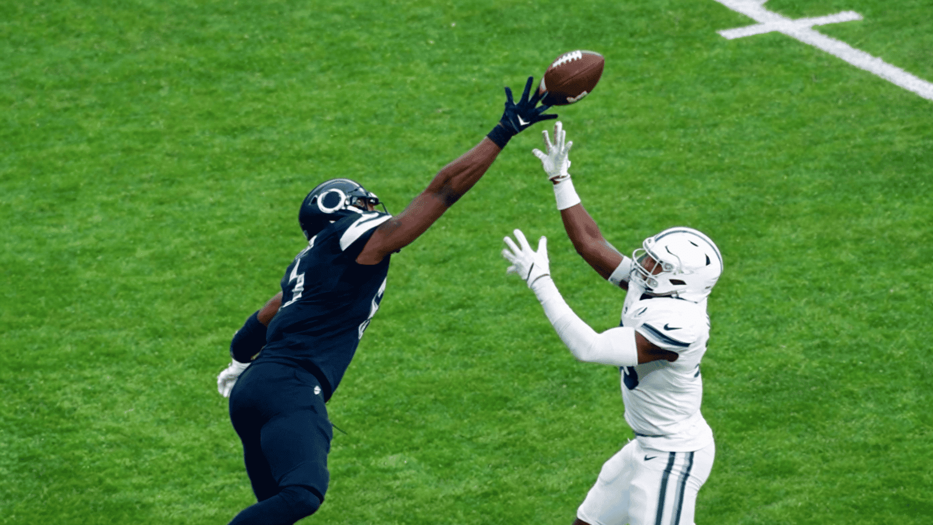 defender reaching up to break up a pass as a receiver attempts to make the catch on a football field