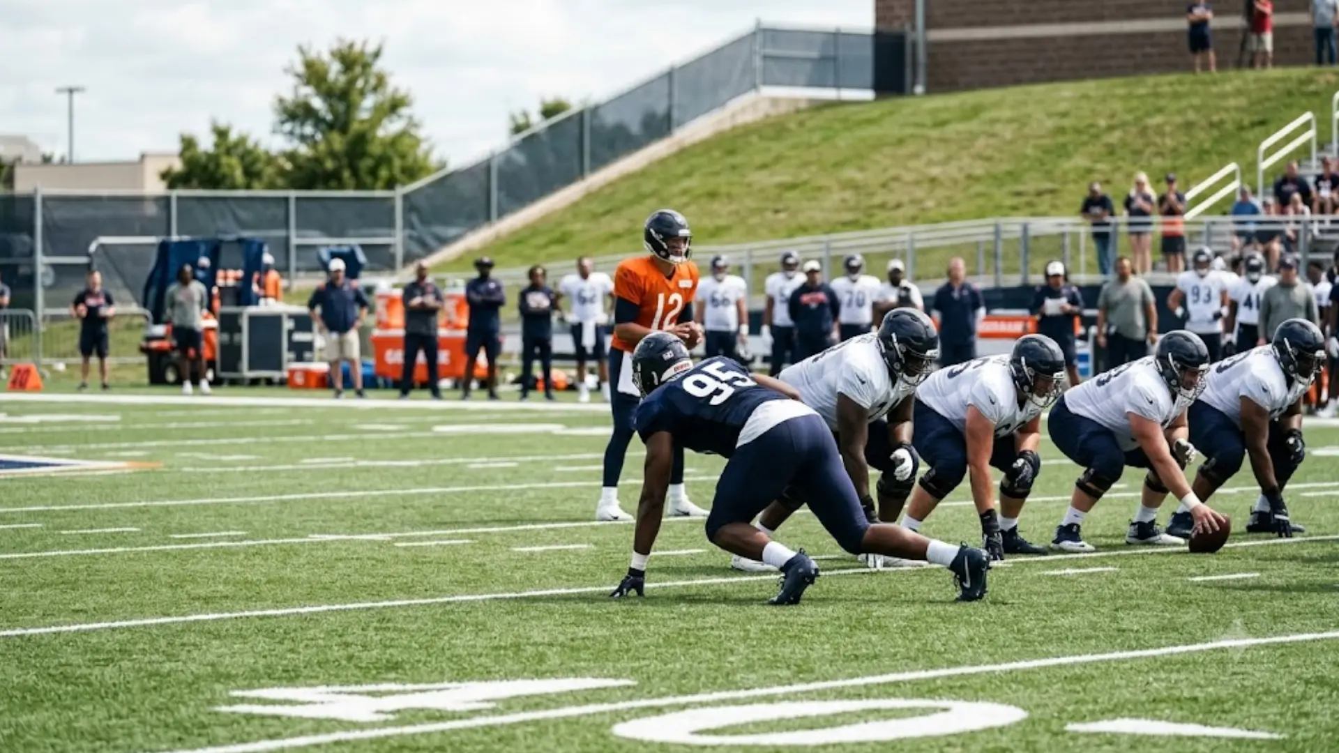 defensive lineman in three point stance across from offensive line during football practice drill with quarterback