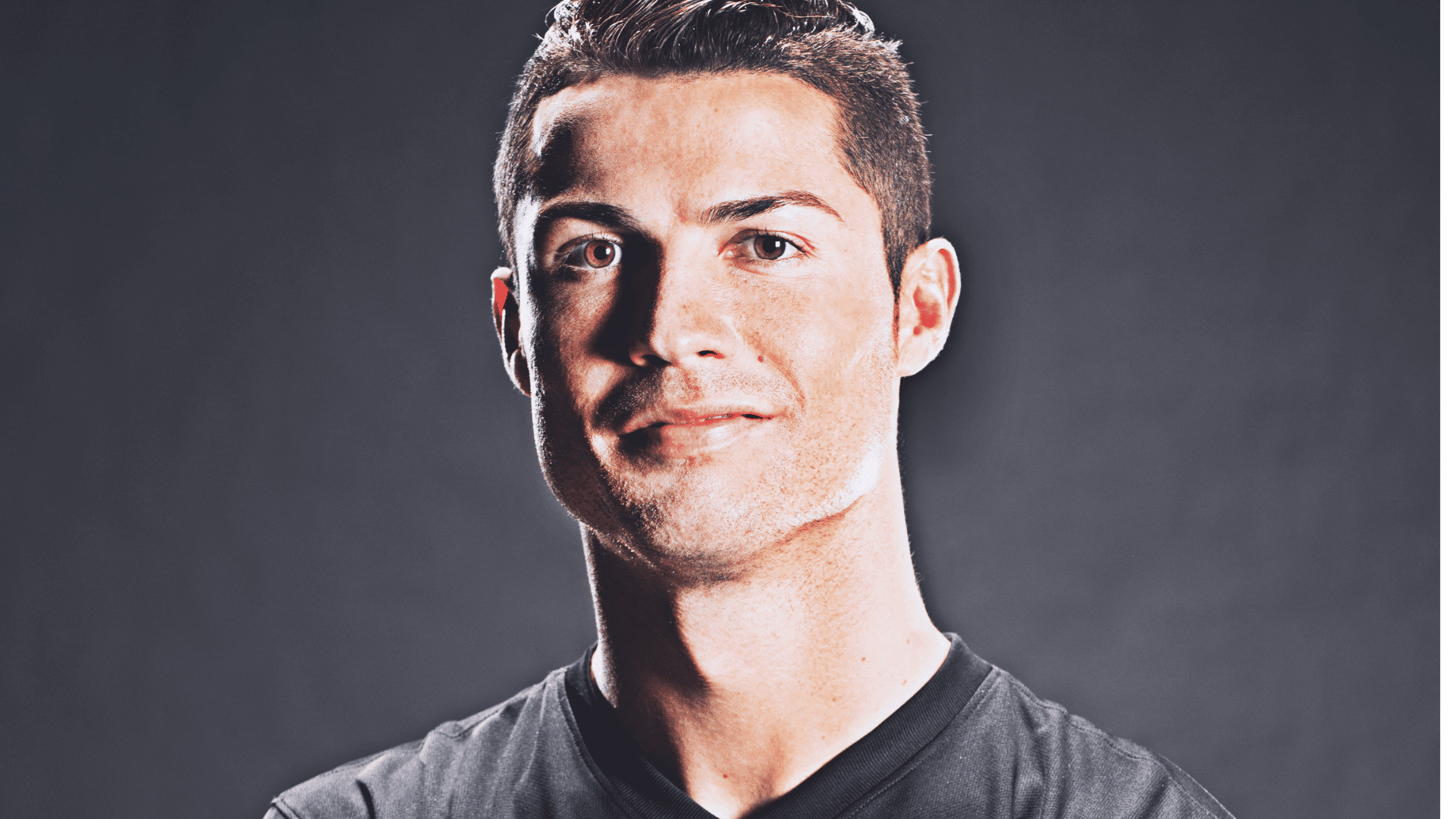 dramatic high contrast portrait of cristiano ronaldo looking forward wearing a dark shirt against a solid grey background