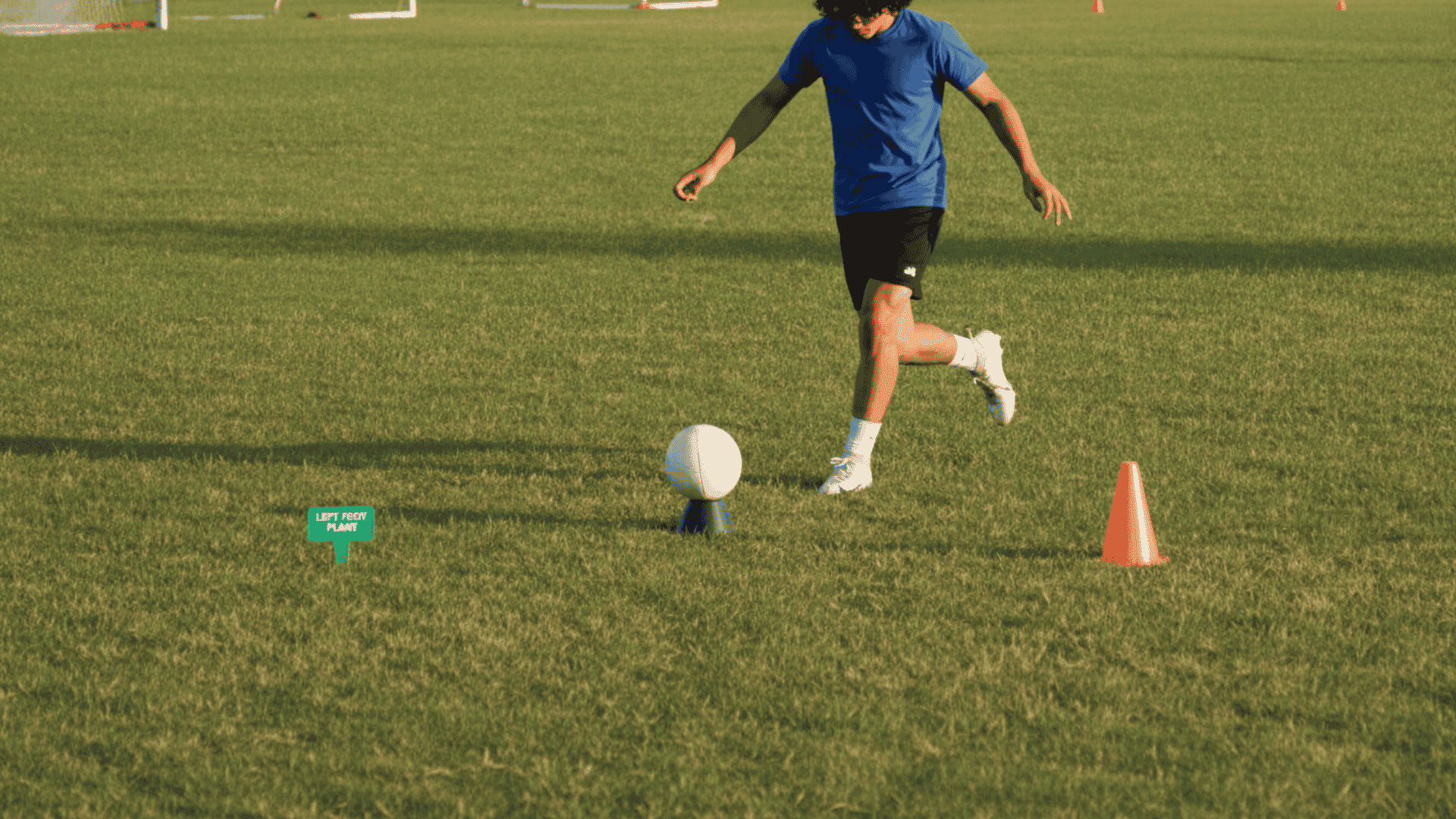 football kicker rehearsing a controlled approach and plant step beside a tee without striking the ball