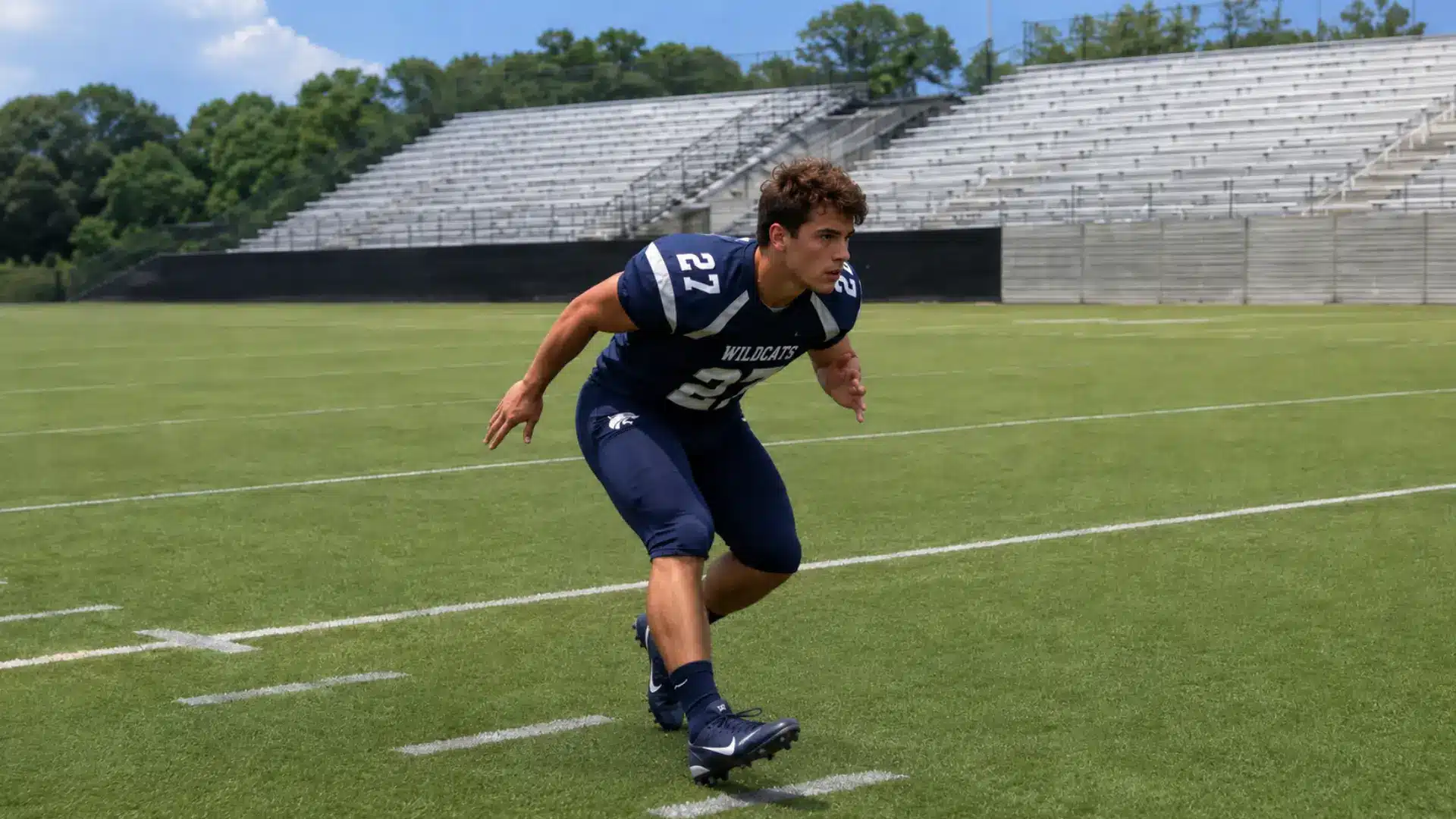 football player backpedals in a defensive coverage stance inside an empty stadium during a practice drill