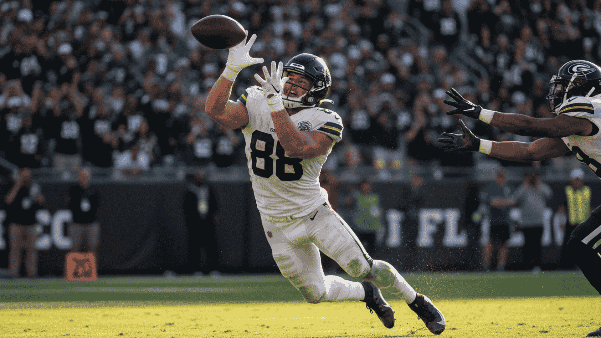 football player diving to catch a pass during a game while a defender reaches from behind