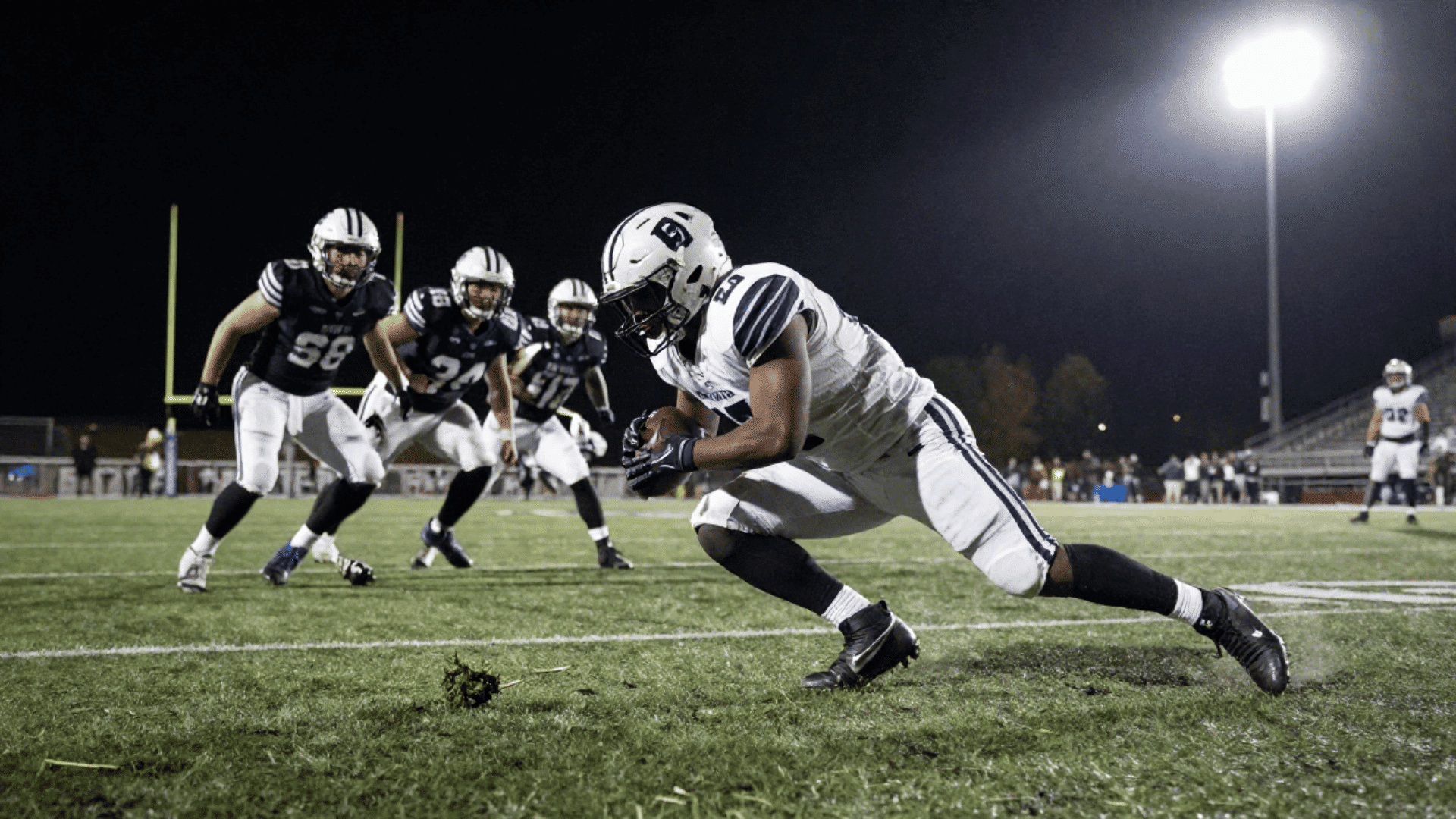 football player in a white uniform with blue stripes lunges forward with the ball about to cross the goal line