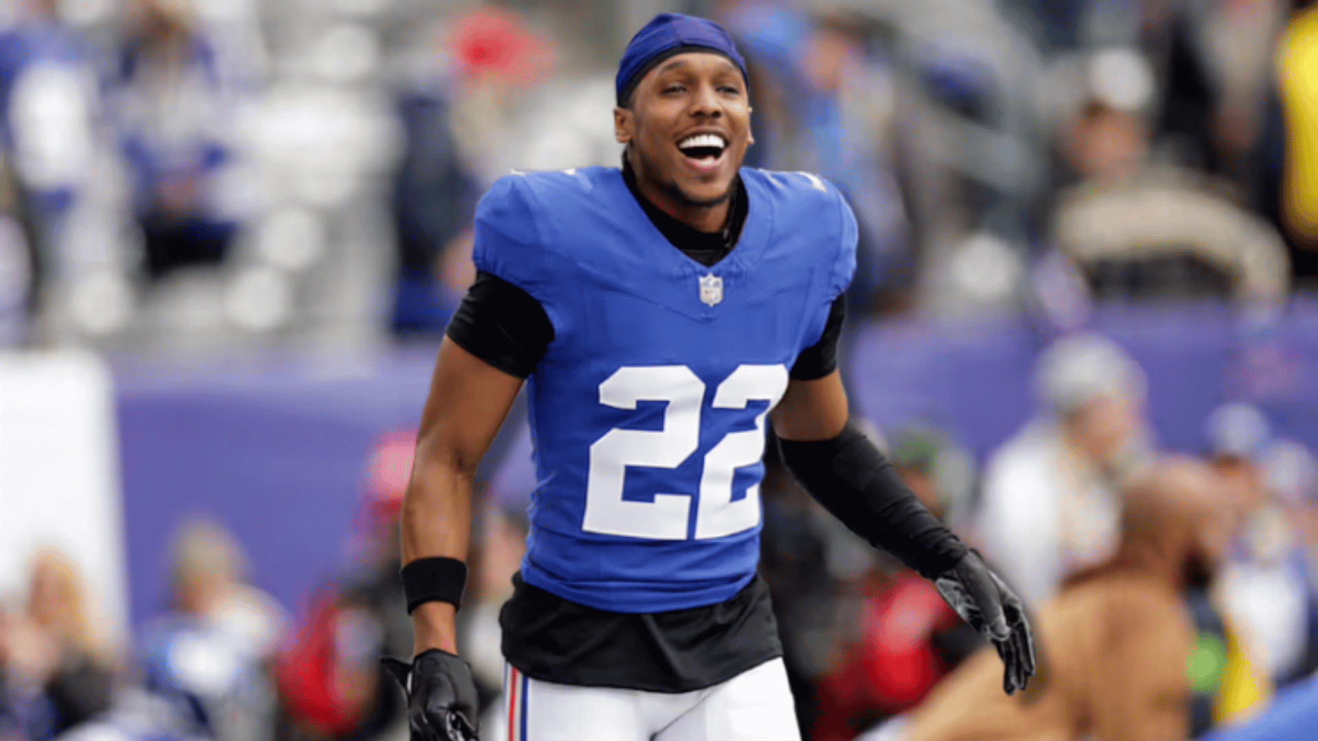 football player in blue number 26 jersey smiling on the field while holding his helmet during a game