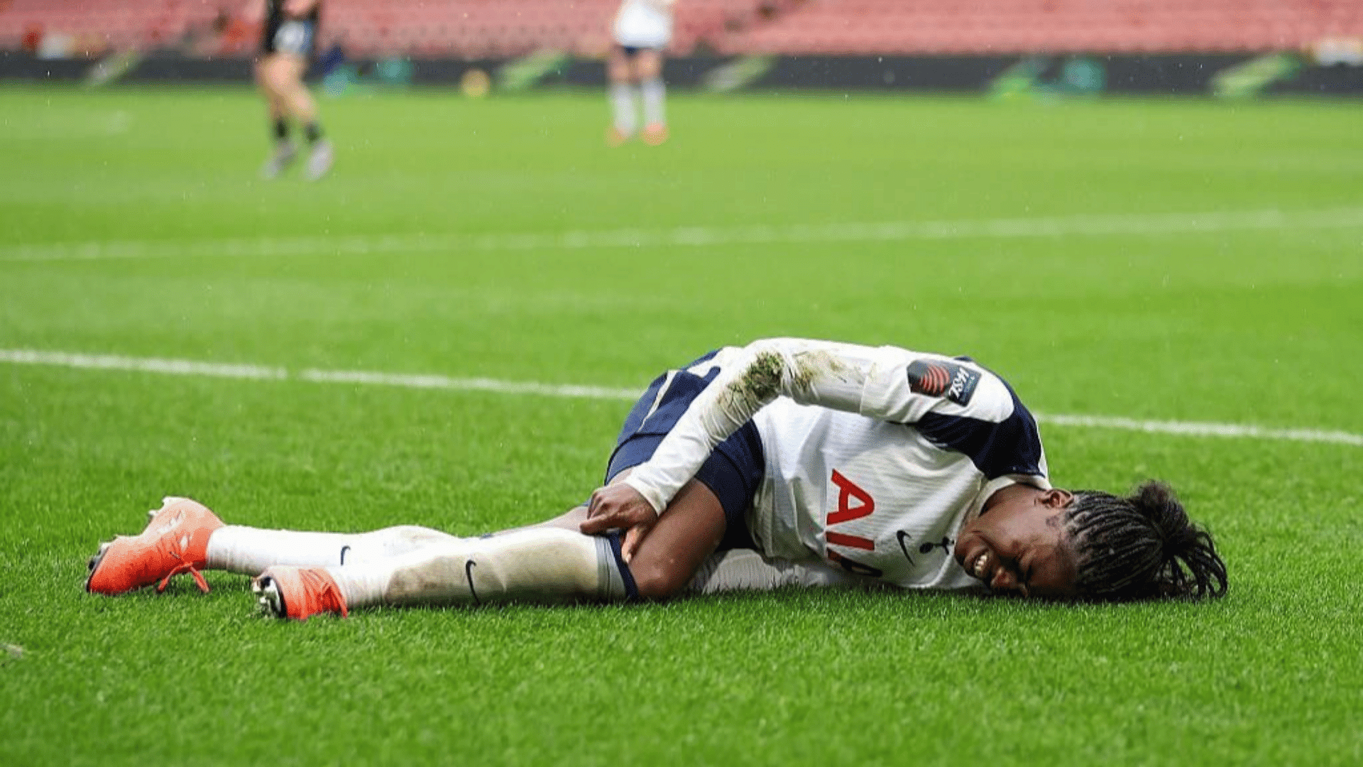 football player in white and navy kit lying on grass holding his thigh in pain during a stadium match