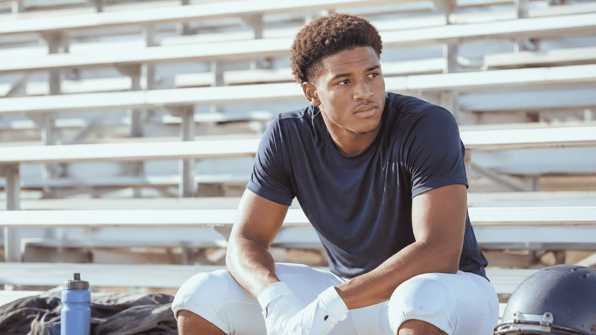 football player sitting on the sideline watching teammates practice during a college football training session