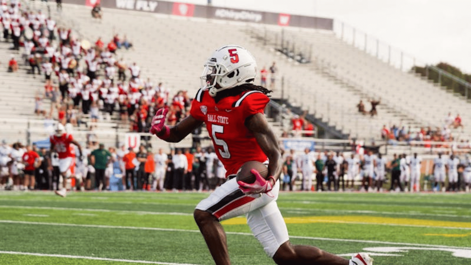 football player wearing a red jersey running down the field during a game situation