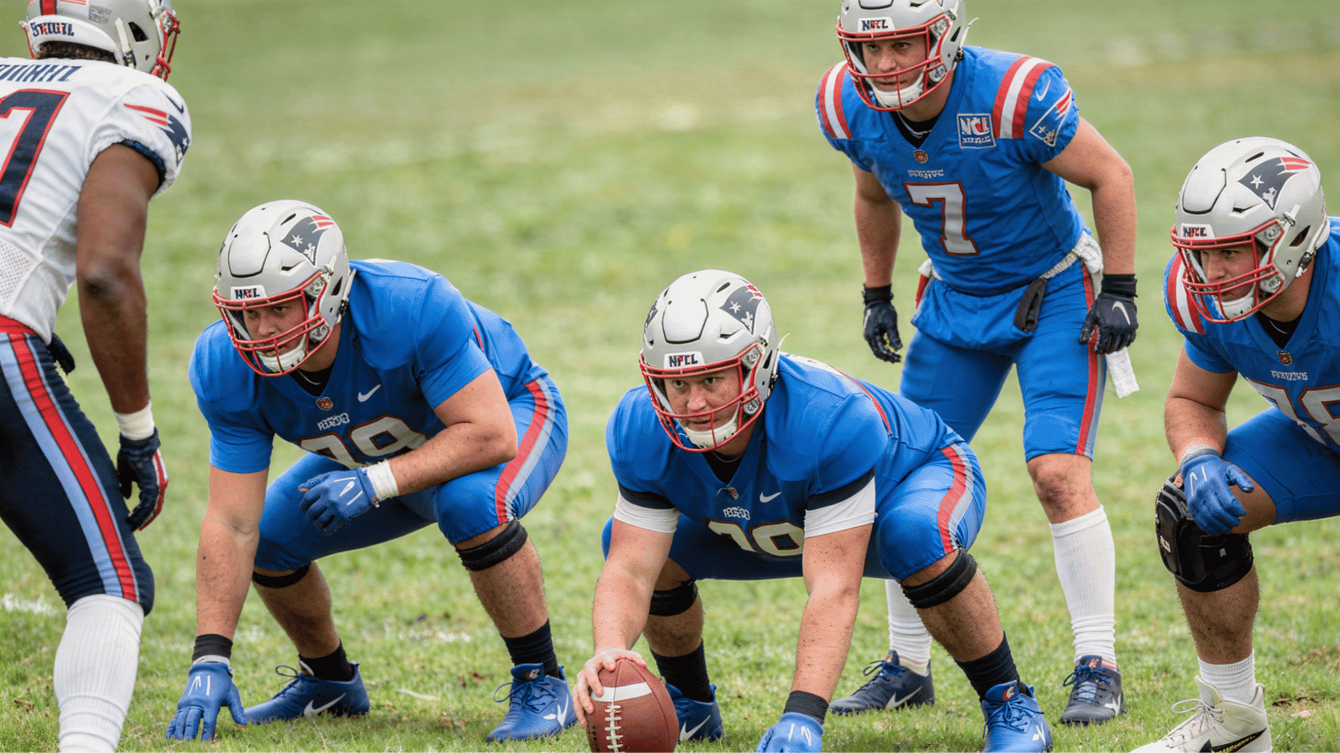 football team in blue uniforms with red and white accents and silver helmets are in a huddle on a grassy field