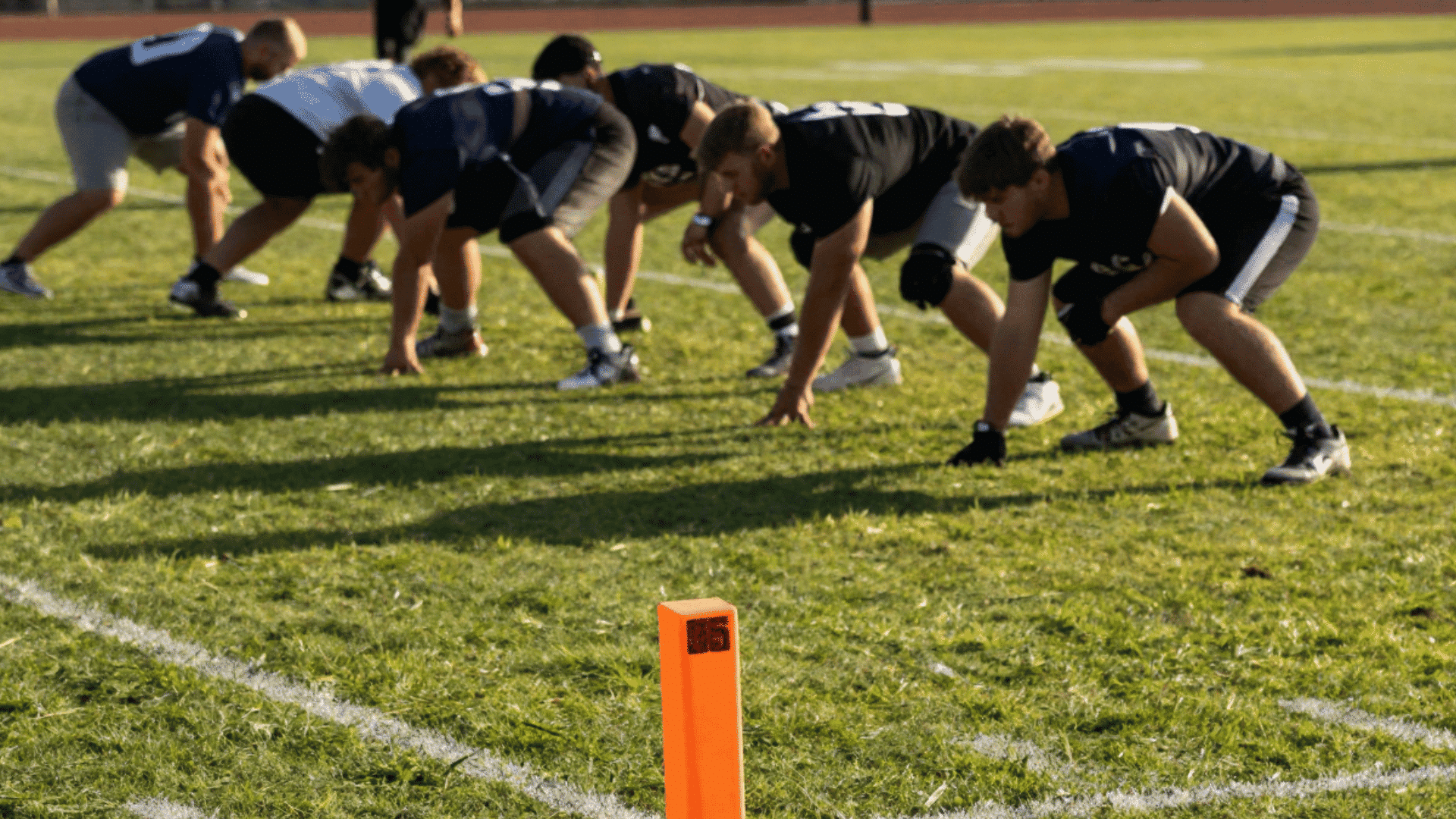 football team lines up on a grassy field with an orange yard marker in the foreground