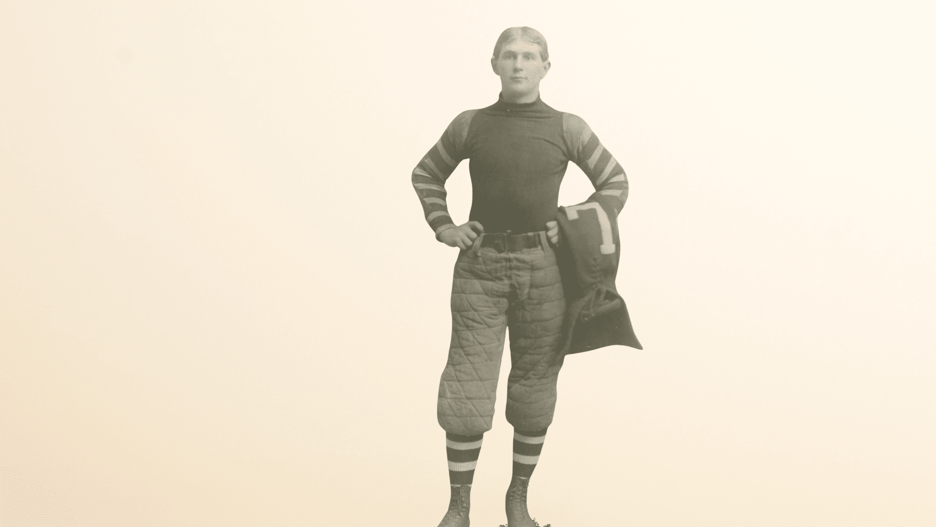 george barclay era football player standing in vintage uniform holding early padded headgear