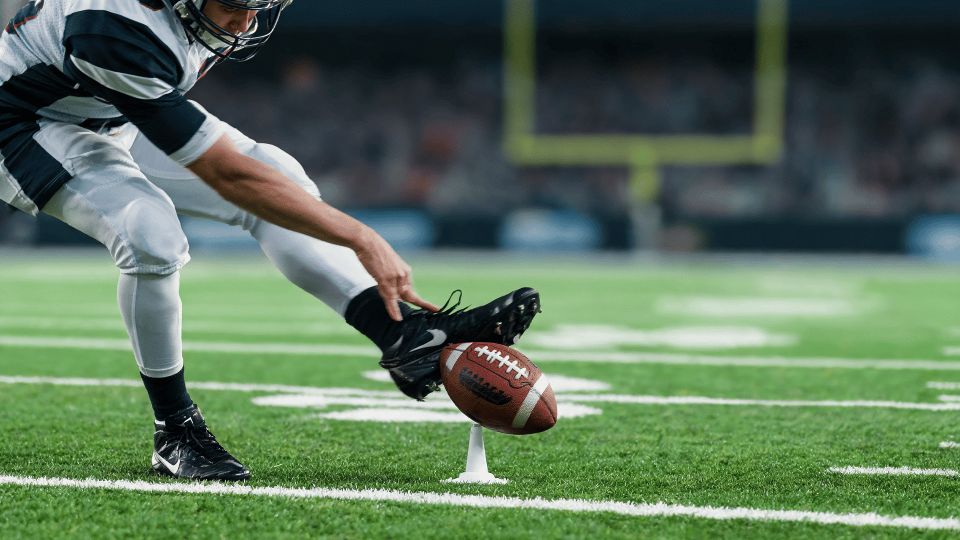high speed side view of a locked ankle striking the lower middle of an american football on a tee