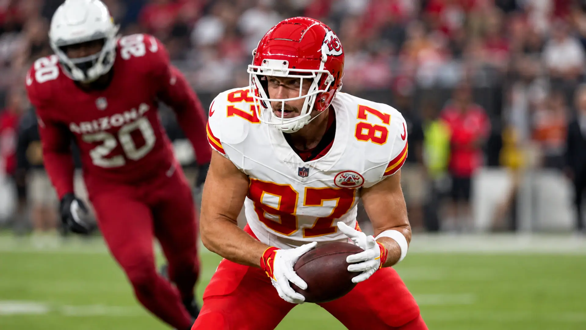 football player grips the ball as a defender closes in from behind during fantasy football game day action