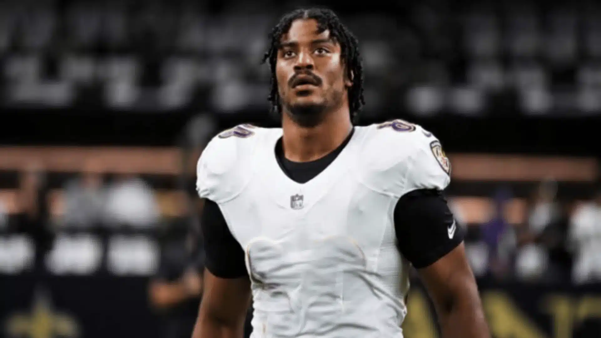 isaiah likely standing on the field in a white baltimore ravens jersey before a game