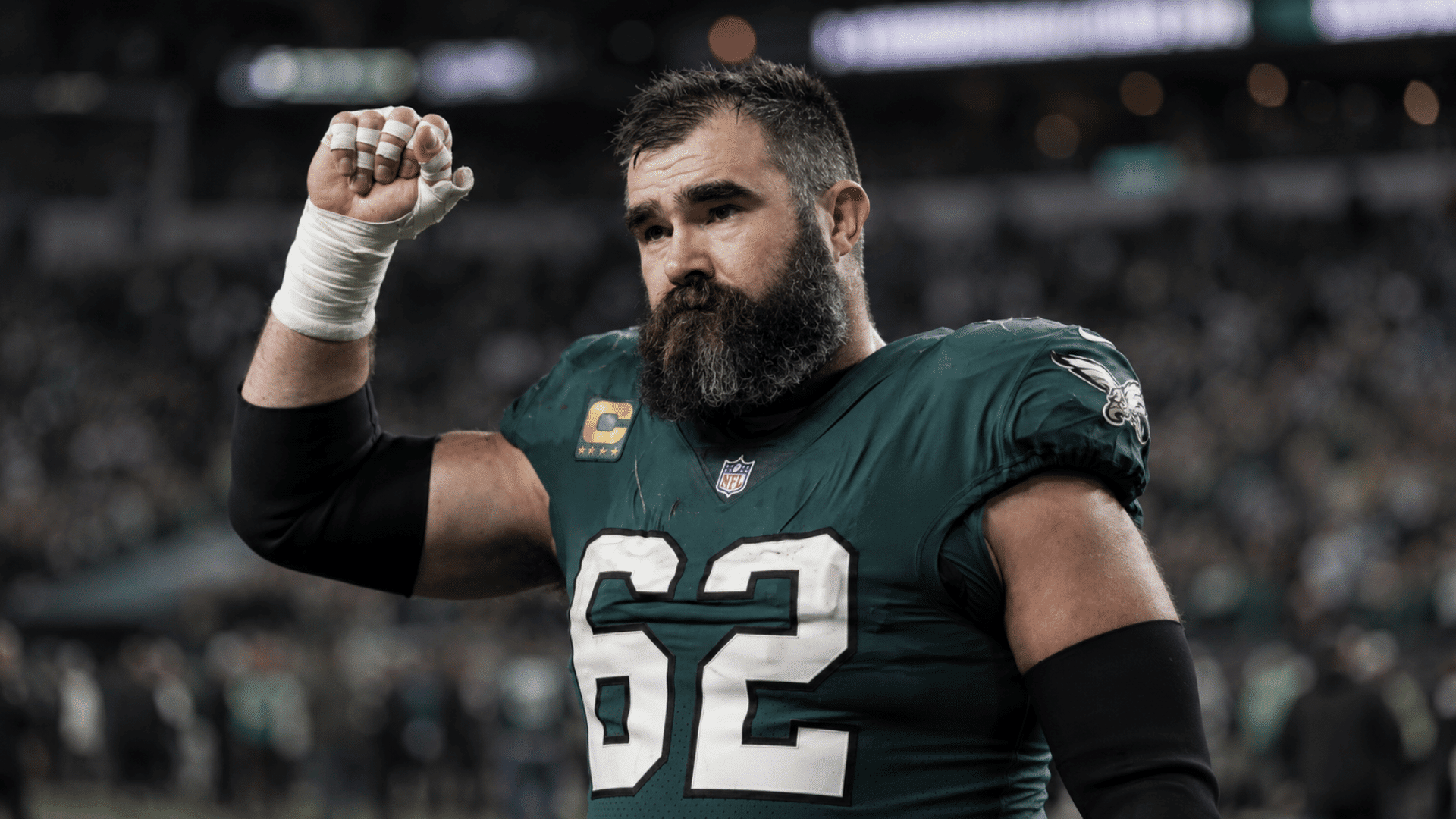 jason kelce raising his fist on the field after a game with stadium lights in the background