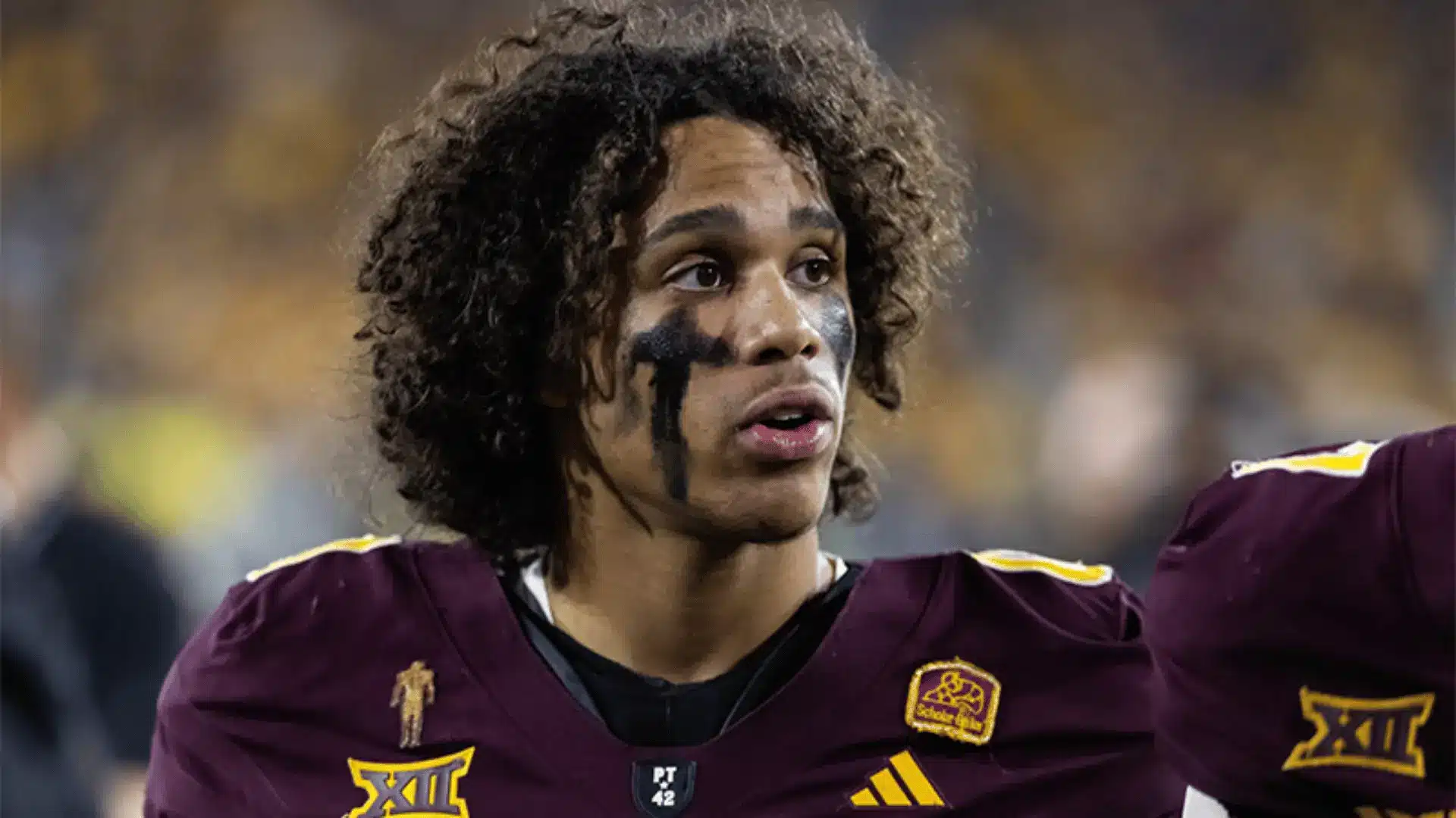 football player in a maroon uniform with eye black looks upward on the field during a game in a stadium