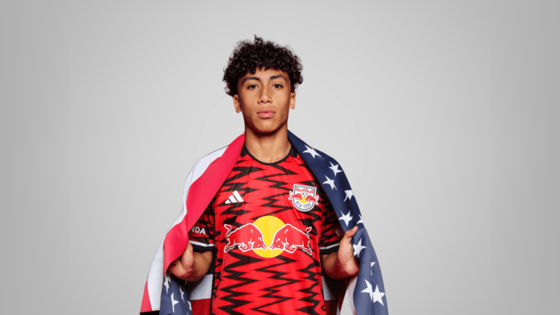 new york red bulls player in red jersey holding an american flag on a clean grey background for match preview