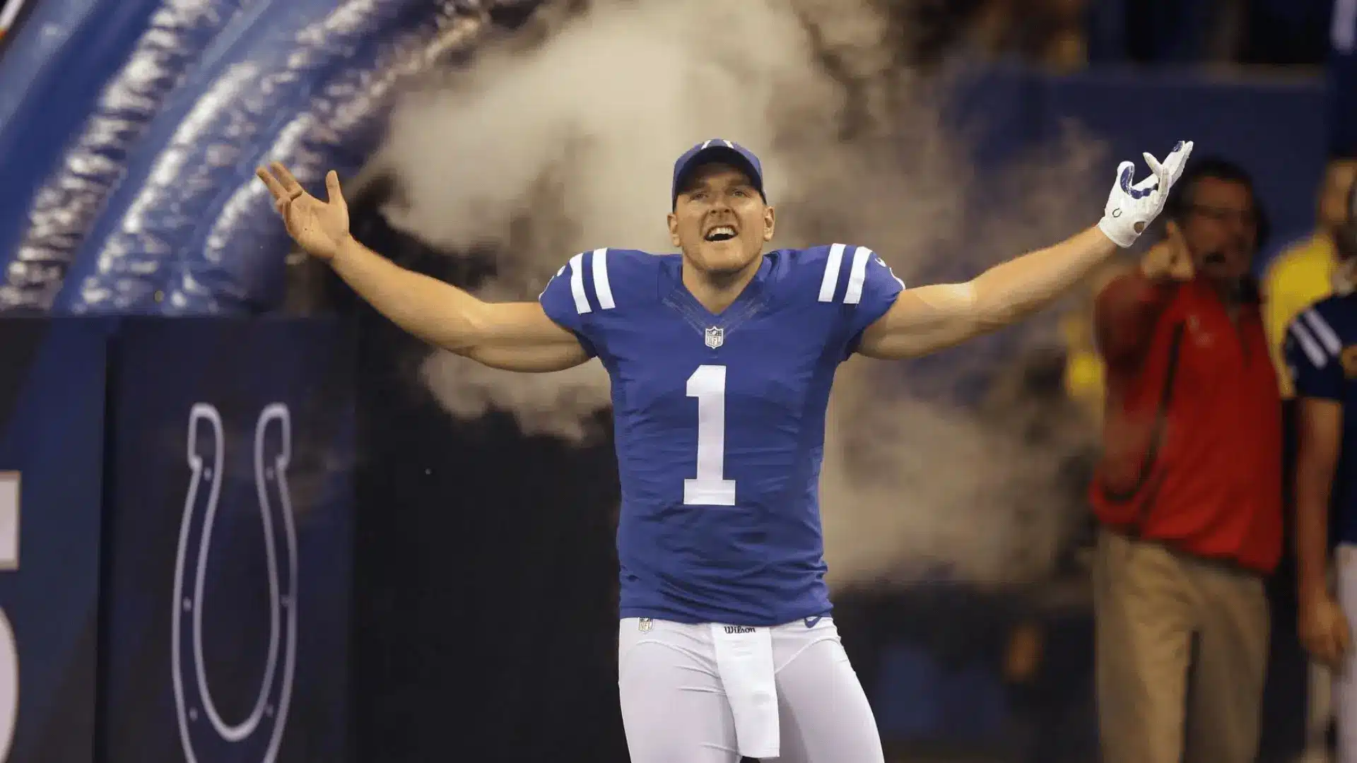an american football player in a blue number one uniform stands with arms spread wide as smoke fills the stadium entrance