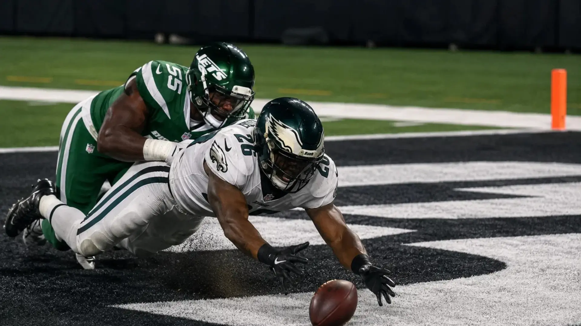 football player losing possession of the ball in the end zone while defenders recover during a live play