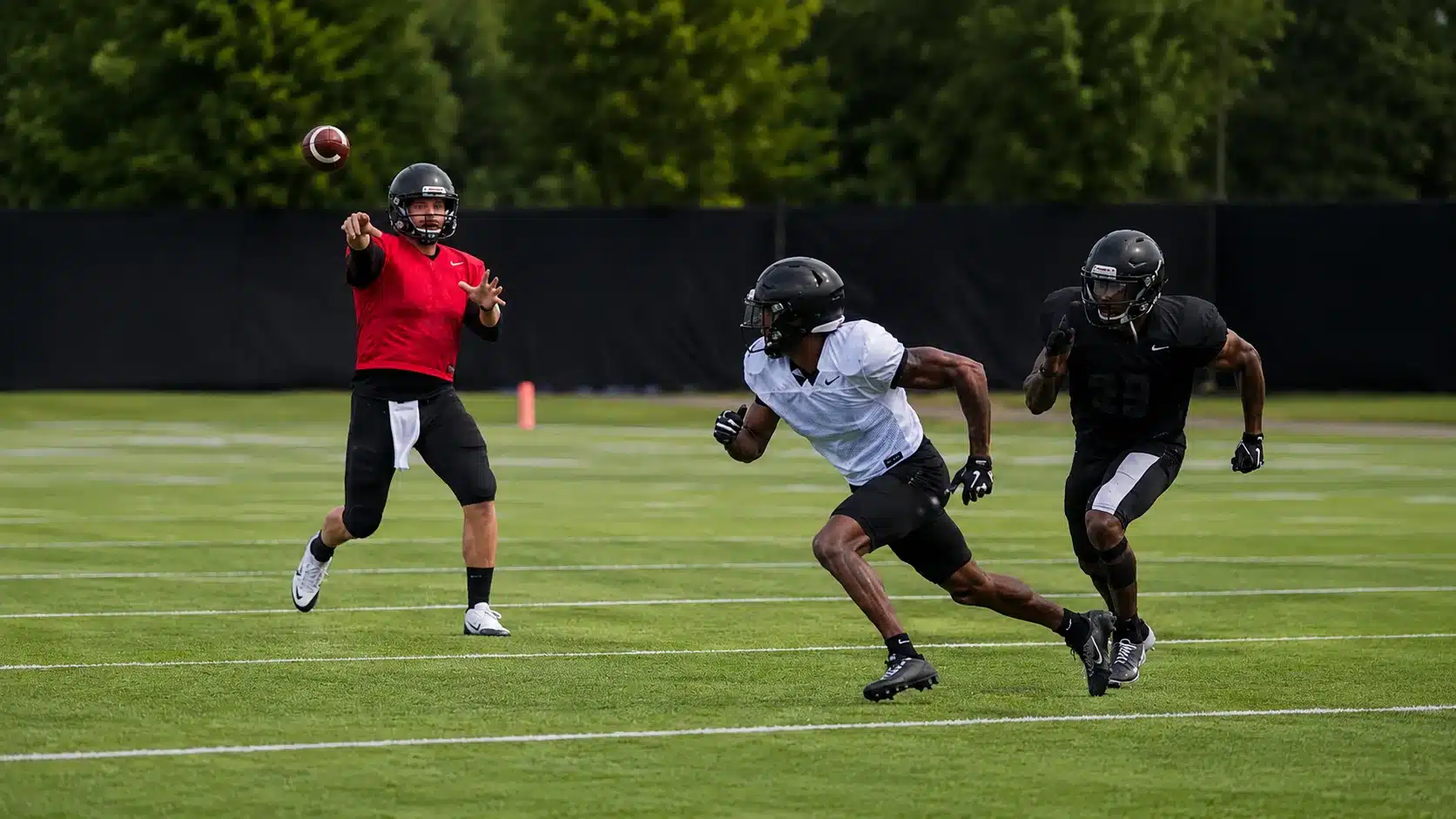 quarterback throws to a receiver crossing the field while a defender trails close behind on turf