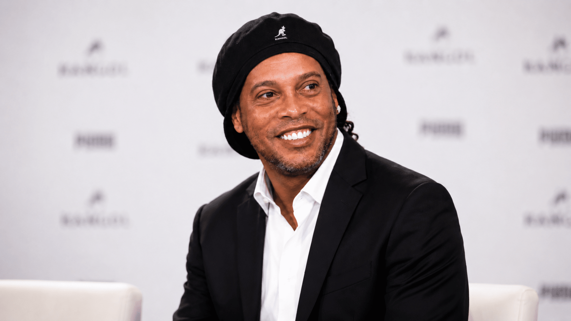 ronaldinho in a navy blazer and white shirt against a softly blurred light background natural lighting