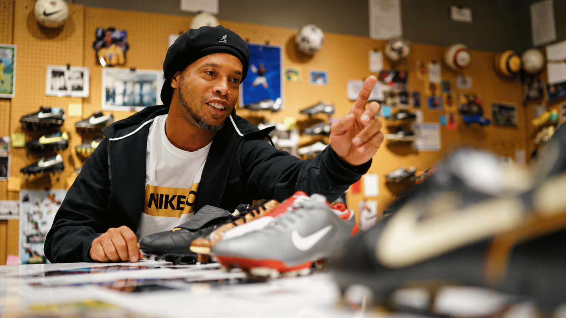 ronaldinho pointing at nike football boots inside a sports store surrounded by footwear displays and memorabilia