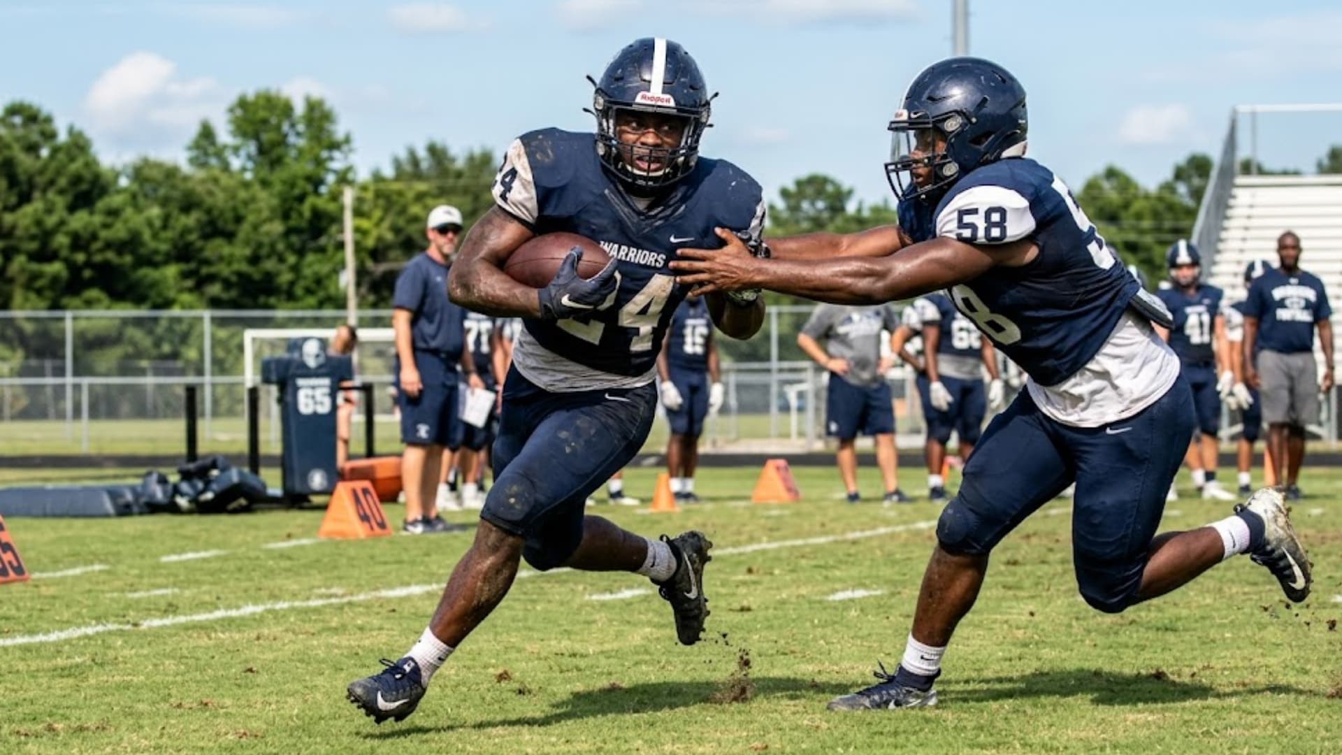 running back carries ball while teammate blocks during team practice drill on field