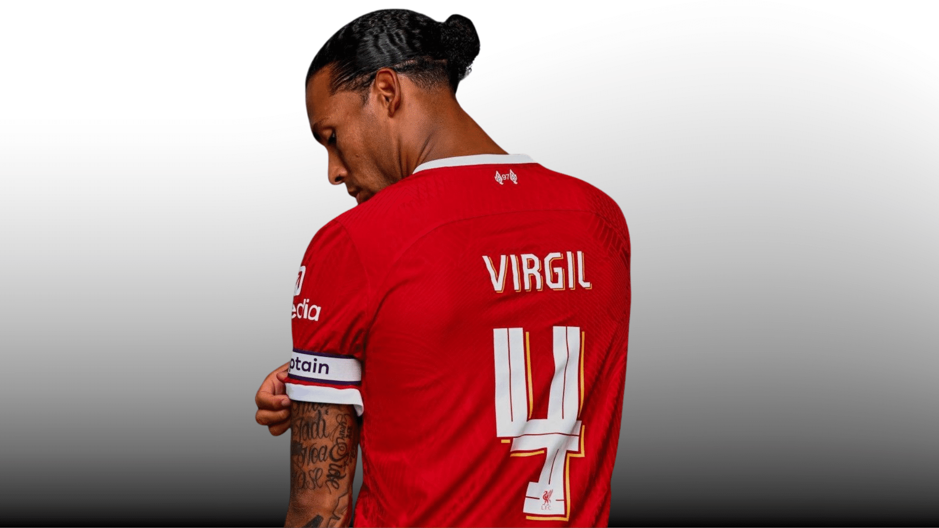 side view of soccer player in red jersey looking down with captain armband on gray gradient background