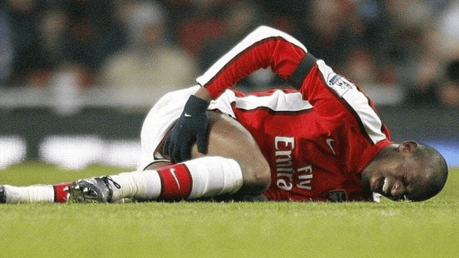 soccer player in a red uniform lies on the field holding his leg with a pained expression during a match